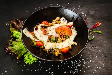 Büyük karidesli bir salata ve siyah arka planda sebze.