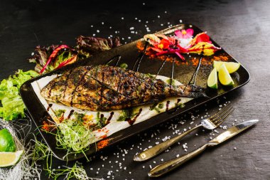 Siyah zemin üzerinde kızarmış balık olan bir yemek.