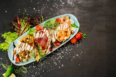 Siyah arka planda karışık et ve sebzeli bir yemek.