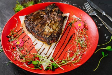 Siyah arka planda kırmızı tabakta kızarmış biftek.