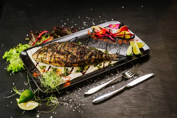 A dish with roasted fish on black background