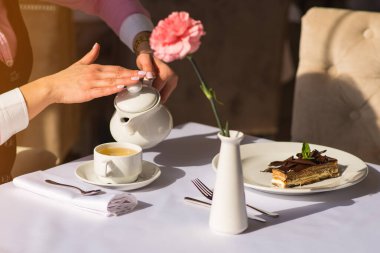 Kadın sabah kahvaltısını yapar ve çaydanlıktan fincana çay döker.