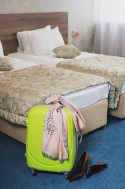 Otel odasında bir bavul ve yatağın yanında ayakkabılar.