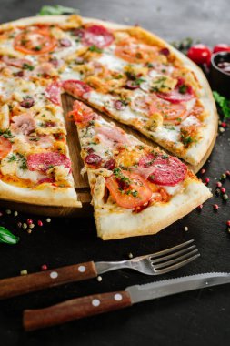 Siyah arka planda salamlı ve jambonlu pizza.