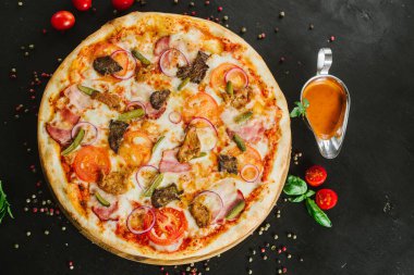 Siyah arka planda çeşitli malzemelerle lezzetli etli pizza.