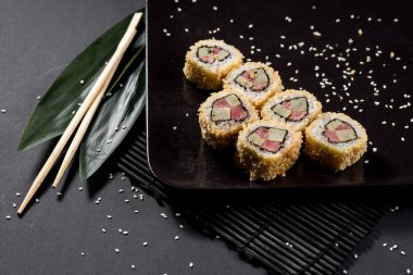 Suşi siyah tabakta bambu yaprakları ve çubuklarla yuvarlanıyor.
