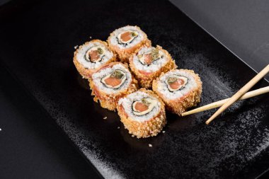 Suşi çubuklarla siyah tabakta yuvarlanıyor.