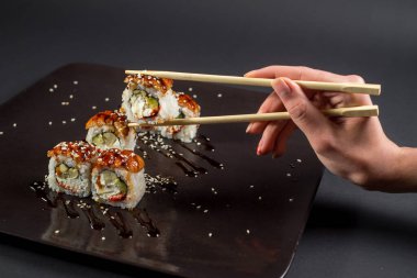 Suşi için yemek çubukları olan bir el koyu arkaplanda bir rulo alıyor.