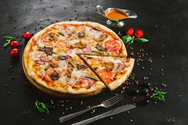 Siyah arka planda çeşitli malzemelerle lezzetli etli pizza.