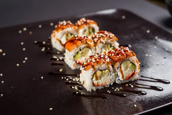 Sushi california roll with sauce and sesame on black plate