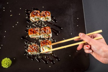 Suşi için yemek çubukları olan bir el koyu arkaplanda bir rulo alıyor.