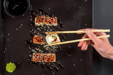 Suşi için yemek çubukları olan bir el koyu arkaplanda bir rulo alıyor.