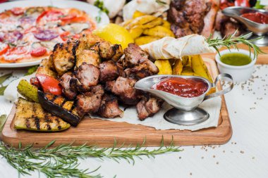 Eti, sebzesi, pizzası ve baharatı beyaz arka planda olan büyük tabaklar.