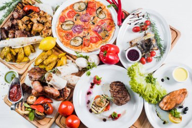 Eti, sebzesi, pizzası ve baharatı beyaz arka planda olan büyük tabaklar.