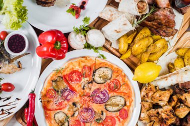 Eti, sebzesi, pizzası ve baharatı beyaz arka planda olan büyük tabaklar.