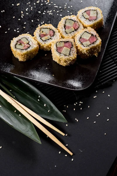 Sushi rolls on black plate with bamboo leaves and chopsticks