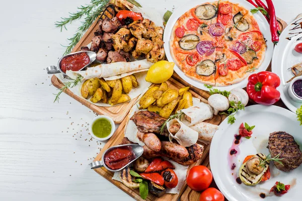Big set of different dishes with meat, vegetables, pizza and spices flatlay on white background
