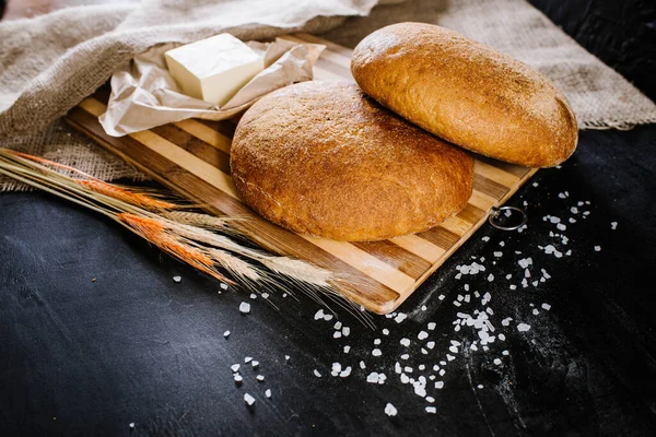 sweet and tasty bread and wheat on black wooden background