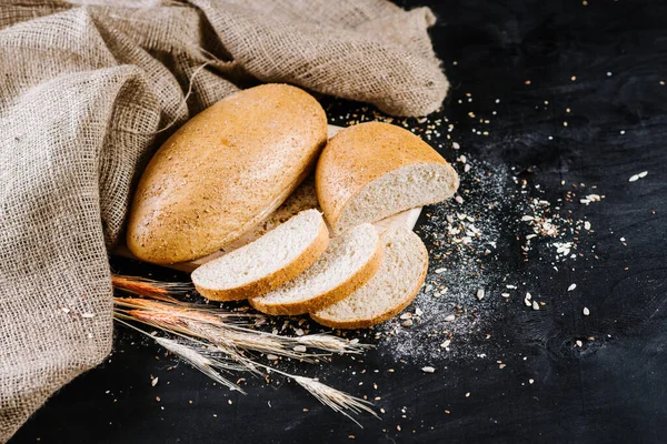 sweet and tasty bread and wheat on black wooden background