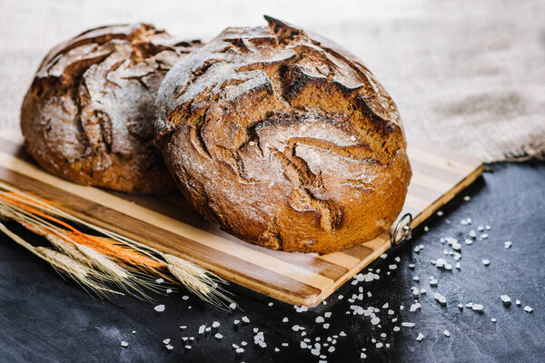 Sweet fresh bread and wheat on black wooden background