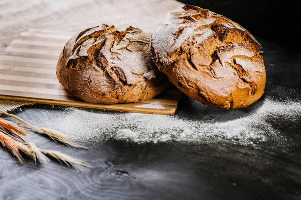 Sweet fresh bread and wheat on black wooden background