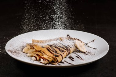 Muzlu krep ve krema tabakta, siyah arka planda yemek çikolatası.