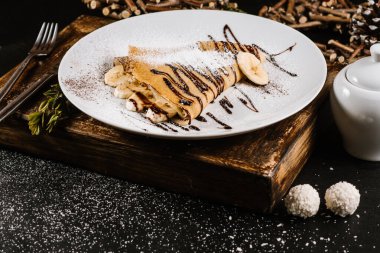 Muzlu krep ve krema tabakta, siyah arka planda yemek çikolatası.