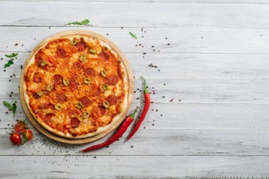 Beyaz ahşap arka planda mozzarella, salam, biber ve zeytinli pizza.