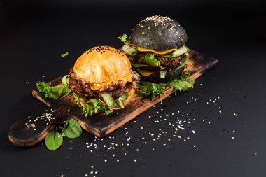 Siyah arka plandaki ahşap masada siyah beyaz ekmekli lezzetli hamburgerler.