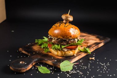 Siyah arka planda ızgara et ve mantarlı lezzetli bir hamburger.