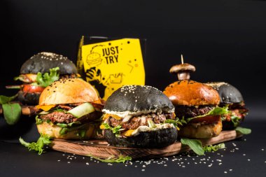 Farklı dolgulu çeşitli hamburgerler ve siyah arka planda susam tohumları.