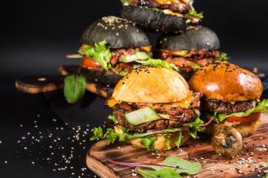 Farklı dolgulu çeşitli hamburgerler ve siyah arka planda susam tohumları.