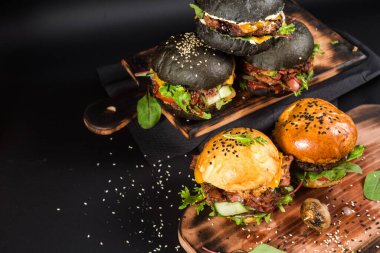 Farklı dolgulu çeşitli hamburgerler ve siyah arka planda susam tohumları.