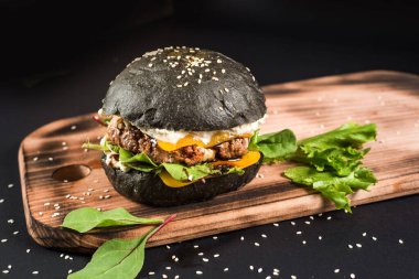 Siyah arka planda siyah çörekli lezzetli hamburgerler.