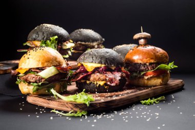 Farklı dolgulu çeşitli hamburgerler ve siyah arka planda susam tohumları.