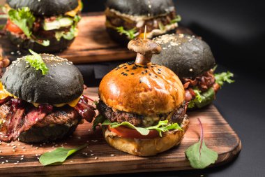 Farklı dolgulu çeşitli hamburgerler ve siyah arka planda susam tohumları.