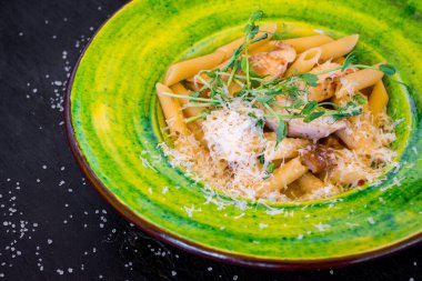 Siyah tahta üzerinde yeşil tabakta peynirli lezzetli makarna.