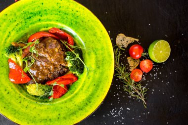 Siyah arka planda yeşil tabakta sebzeli et garnitürü