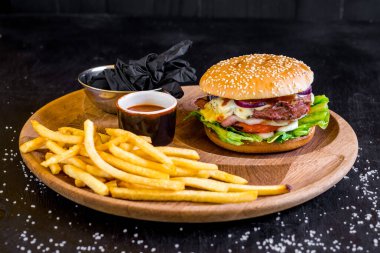 Peynirli lezzetli burger ve siyah tahta üzerinde kızarmış patates.