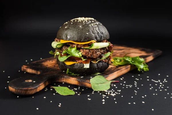 Tasty craft burger with black bun on the black background