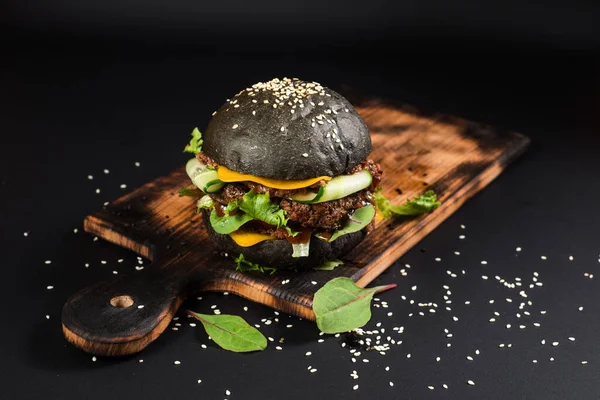 Tasty craft burger with black bun on the black background