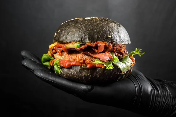 Big black hamburger in hand on the black background