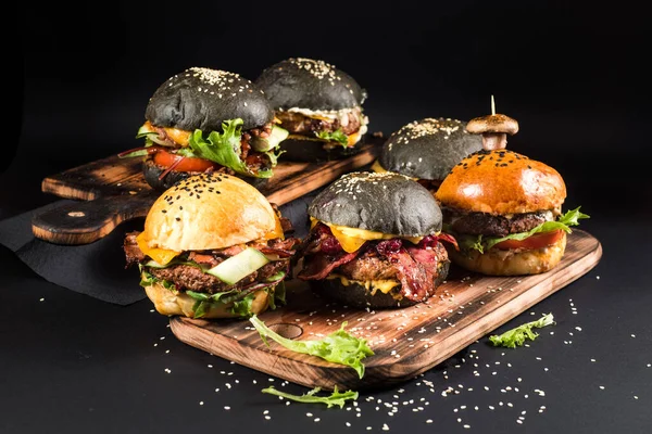 Farklı dolgulu çeşitli hamburgerler ve siyah arka planda susam tohumları.