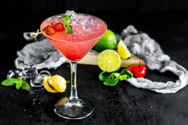 Pink cocktail with cherry and ice on black background