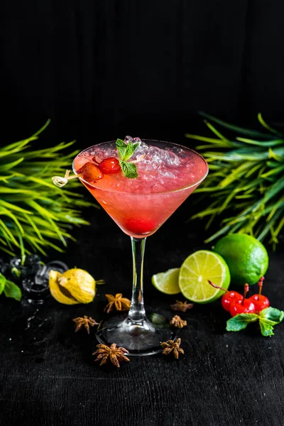 Pink cocktail with cherry and ice on black background