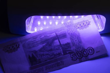 Kızılötesi ışıkta beş bin Rus rublesi. Detektöre bak. Sahte mi gerçek mi diye kontrol et. Sahte banknotlar basmak, bankayı 5000 ruble 'lik bir kasiyerle kontrol etmek, bir bankacı tarafından. Finansal, bankacılık kavramı.