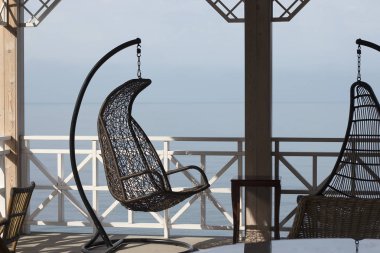 Deniz manzaralı, hasır renkli sallanan sandalye. Denizde dinlenmek, turizm ya da tatillerde seyahat etmek. Deniz kenarında yaz terası.