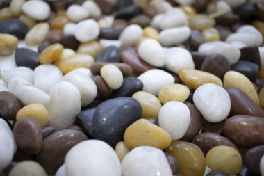 Renkli, yuvarlak çakıl taşları. Siyah, beyaz, sarı, güneş ışığında çok renkli. Arkası bulanık, arkası soyut, tasarımcı bokeh arkaplanı. Sahilde renkli çakıl taşları var..