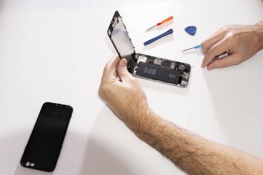 Hands repair the phone, hold a protective glass matrix. Dismantling glass from a mobile phone. Phone repair in a service center.