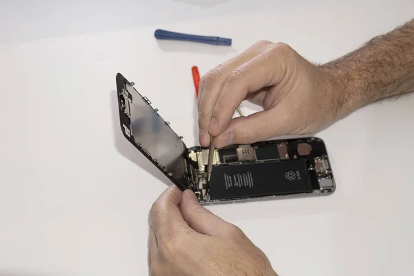 Screws are unscrewed with a screwdriver tool. Replacing the touch matrix of the glass touchpad. Phone repair in a service center. Men's hands are repairing a mobile phone.